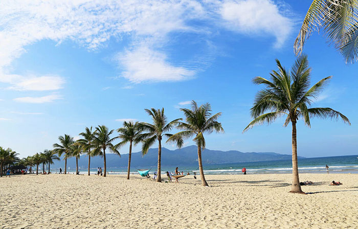 My Khe Beach à Da Nang Immense plage avec des surfeurs et vue sur les montagnes.